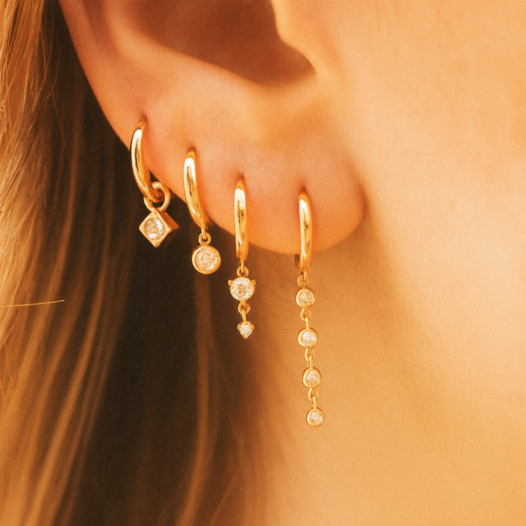 Close-up of a person wearing gold hoop earrings with small diamond-like stones.